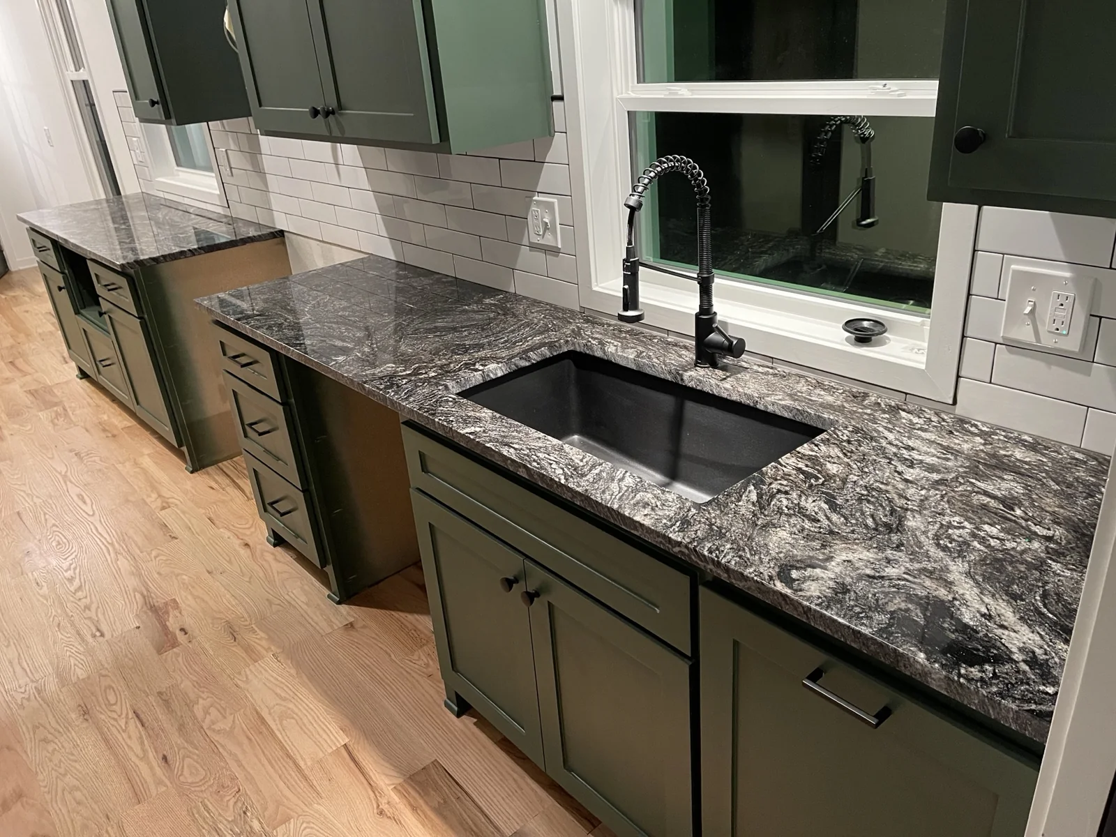 Black and white granite countertops with green cabinets and black sink by KC Cabinetry & Stone