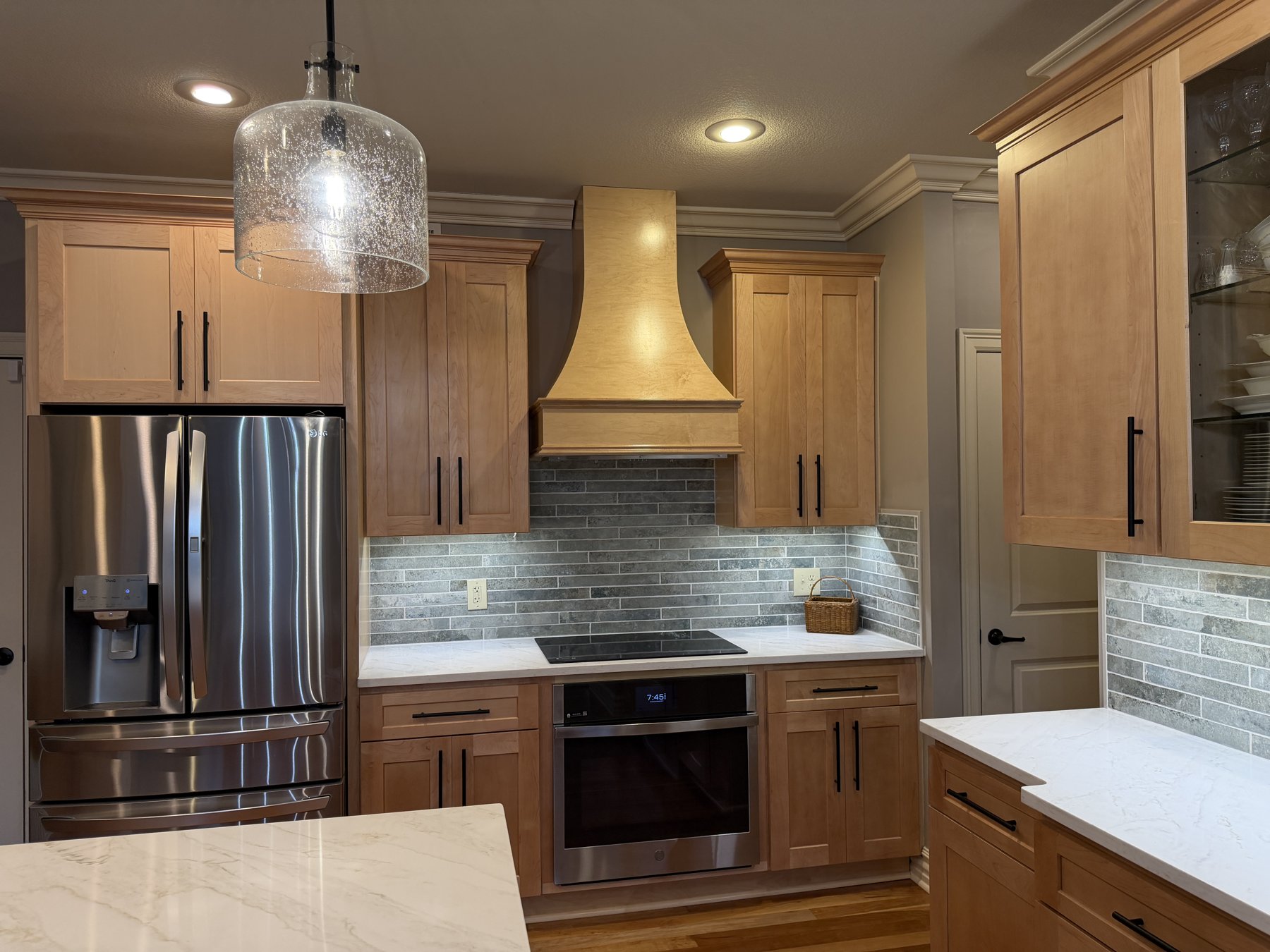 Relocated oven and cooktop with custom maple hood and tile backsplash in a Lee's Summit, MO kitchen